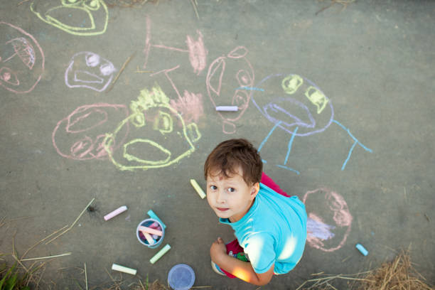 Boy draws with chalk on the pavement around the house