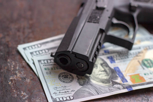 미국 달러 배경에 검은 총. 군사 산업, 전쟁, 글로벌 무기 무역, 무기 판매, 계약 살인 및 범죄 개념 - currency crime gun conflict 뉴스 사진 이미지
