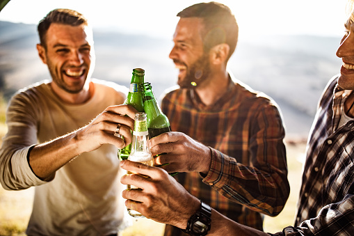 Close up of cheerful male friends having fun while toasting with beer outdoors.