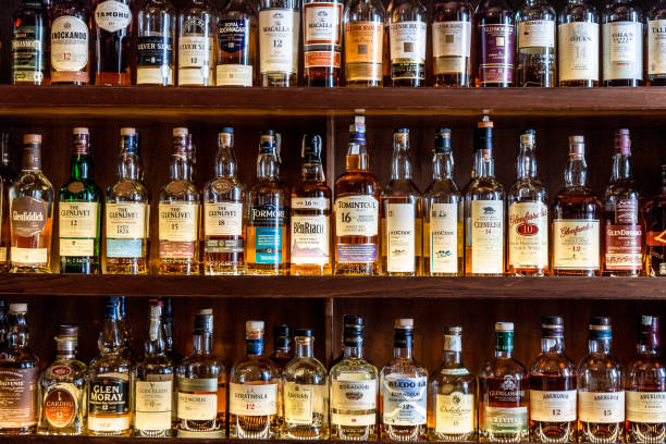 Large selection of Scottish malt whisky at the bar London, UK - 10 May, 2019: Color image depicting a huge selection of different malt Scotch whisky bottles in a row and displayed on wooden shelves at a bar in London, UK. The whisky is mainly Scottish single malt and comes from a range of different distilleries. Room for copy space. scottish highlands photos stock pictures, royalty-free photos & images