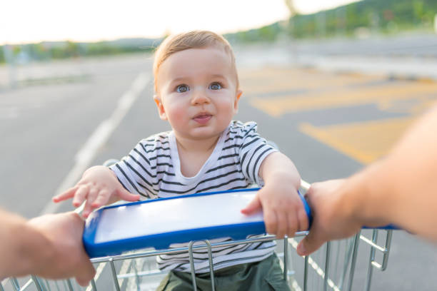 Beautiful and adorable baby in shopping cart. Beautiful and adorable baby in shopping cart. Father and son in shopping. Baby boy sitting in the shopping trolley outside. Family, childhood, fatherhood and people concept supermarket family retail cable car stock pictures, royalty-free photos & images