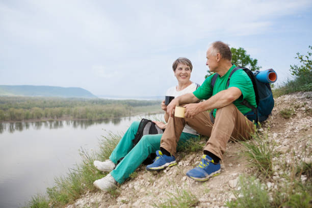 elderly couple with backpacks travels around mountains. senior couple walking in nature - couple walking old middle imagens e fotografias de stock