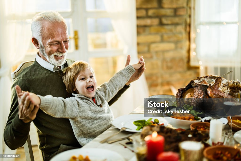 Feliz abuelo y nieto divirtiéndose durante el almuerzo de acción de gracias en casa. - Foto de stock de Día de Acción de Gracias libre de derechos