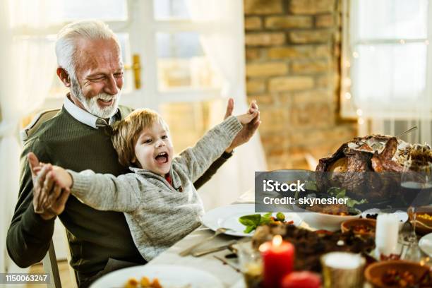 Feliz Abuelo Y Nieto Divirtiéndose Durante El Almuerzo De Acción De Gracias En Casa Foto de stock y más banco de imágenes de Día de Acción de Gracias