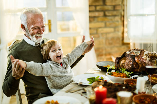 szczęśliwy dziadek i wnuk zabawy podczas lunchu dziękczynienia w domu. - dining table child grandparent grandchild zdjęcia i obrazy z banku zdjęć