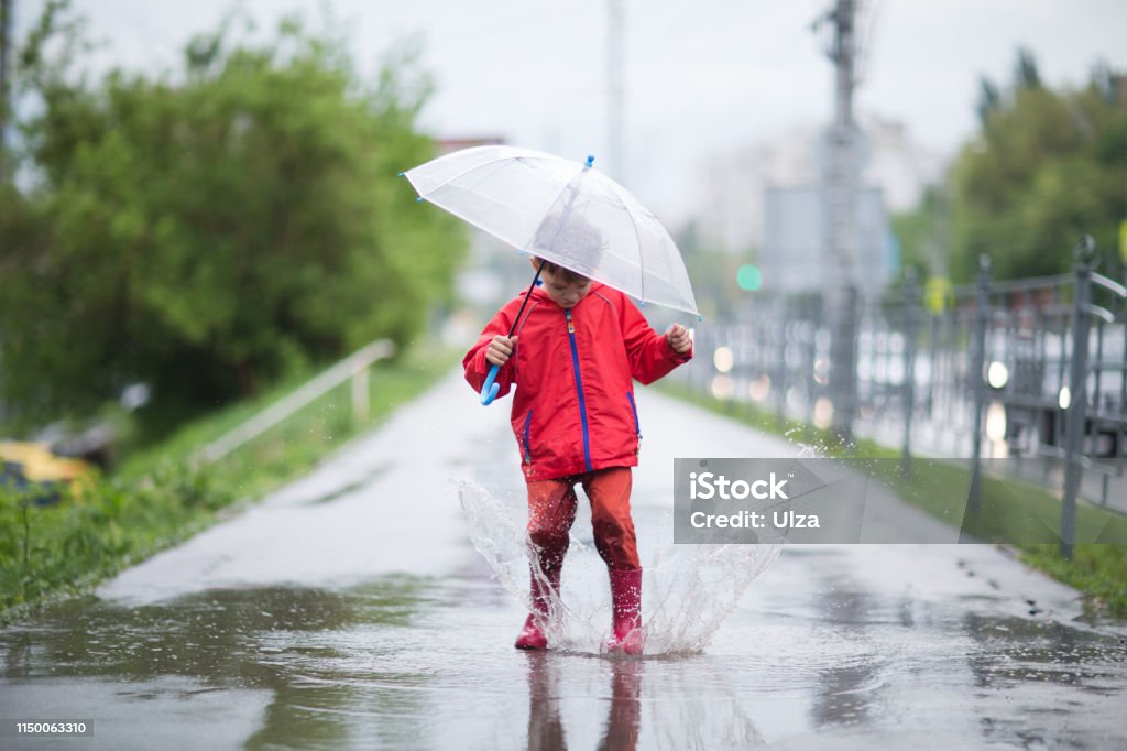 little child boy with an umbrella playing out in the rain in the summer outdoors Beauty Stock Photo