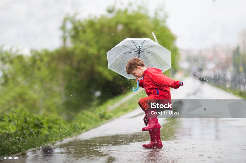 little child boy with an umbrella playing out in the rain in the summer outdoors Child Stock Photo