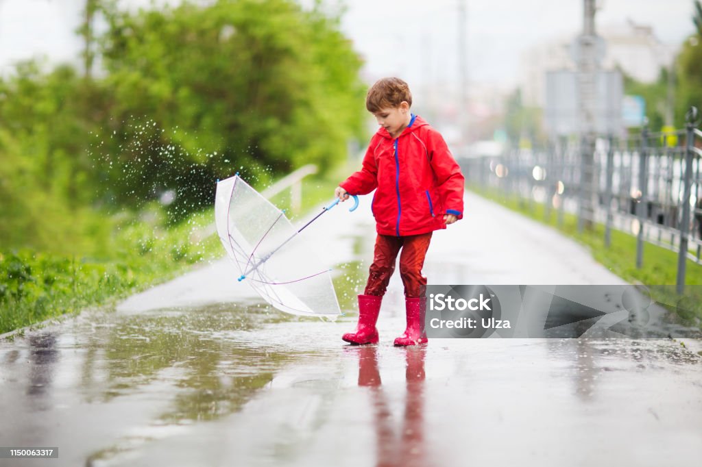 little child boy with an umbrella playing out in the rain in the summer outdoors Beauty Stock Photo