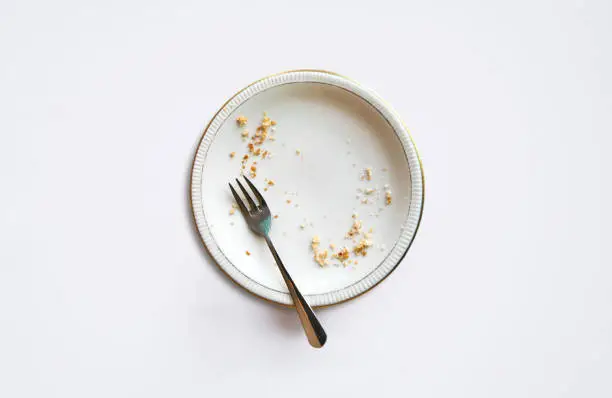 Empty plate with crumbs after eating on a white background. The concept of the end of the holiday or celebration.