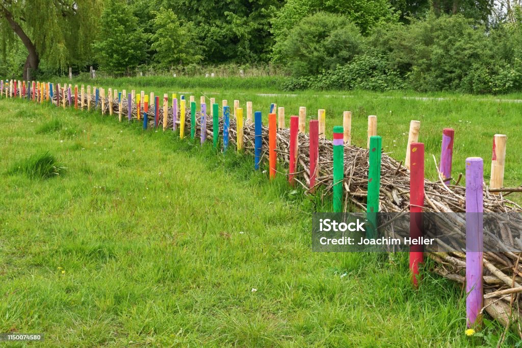 A filled fence made of colorfully painted round timber palisades. Creative example of a community garden, designed by children. Landscape Backgrounds Stock Photo