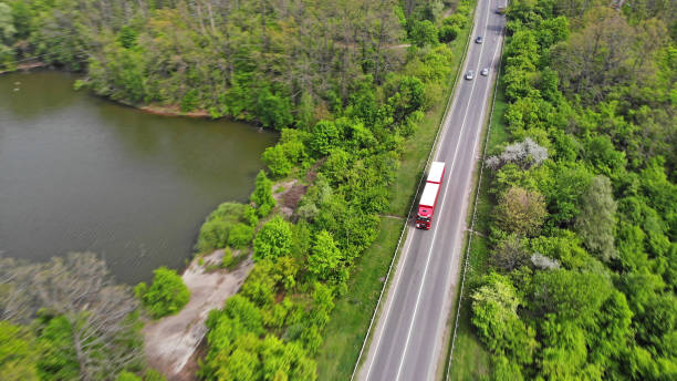 istock Transport logistics background with trucks on a highway between green forest and lake 1150074979