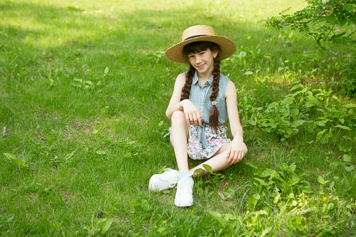smiling little girl with hat sitting on green grass in the park