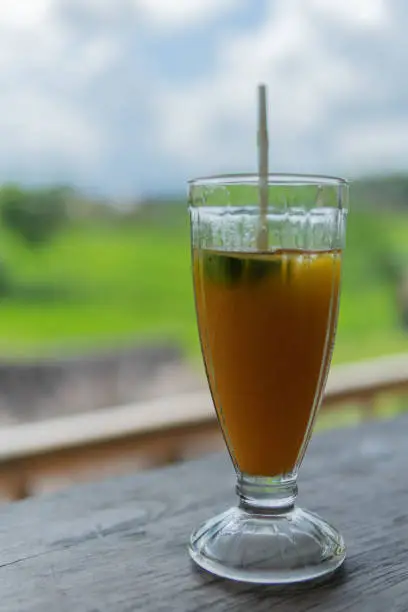 Photo of Mango papaya banana iced drink with rice fields in the background.