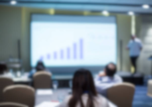 istock Blurred business presentation with corporate speaker near blank white screen. Seminar concept background with executive leading workshop in conference hall. Presenter in lecture to audience. 1150089053