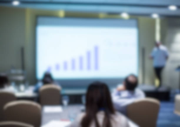 Blurred business presentation with corporate speaker near blank white screen. Seminar concept background with executive leading workshop in conference hall. Presenter in lecture to audience. stock photo