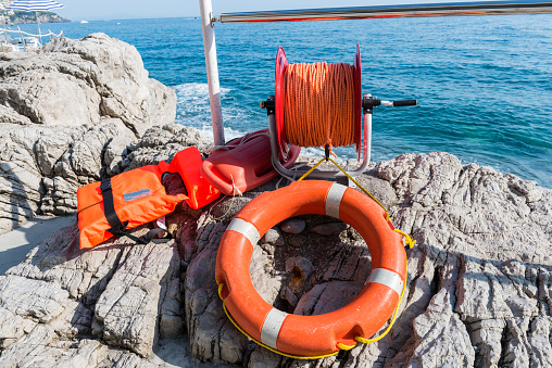 Orange lifebuoy with rope and life jacket on the rocks near sea