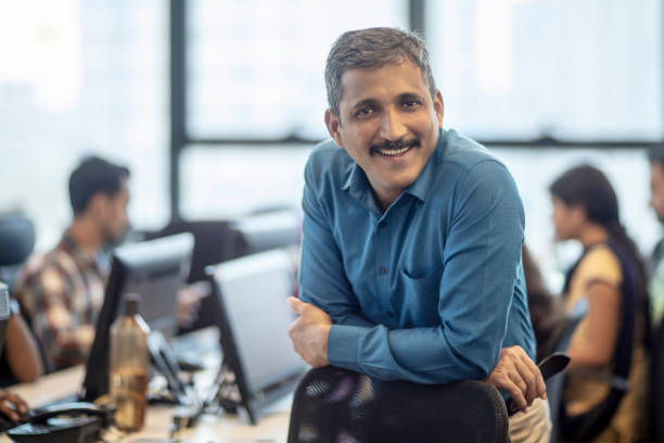 Smiling mature manager sitting at creative office Portrait of smiling mature manager leaning on chair. Confident male entrepreneur is at creative office. He is in formalwear. Indian Ethnicity stock pictures, royalty-free photos & images