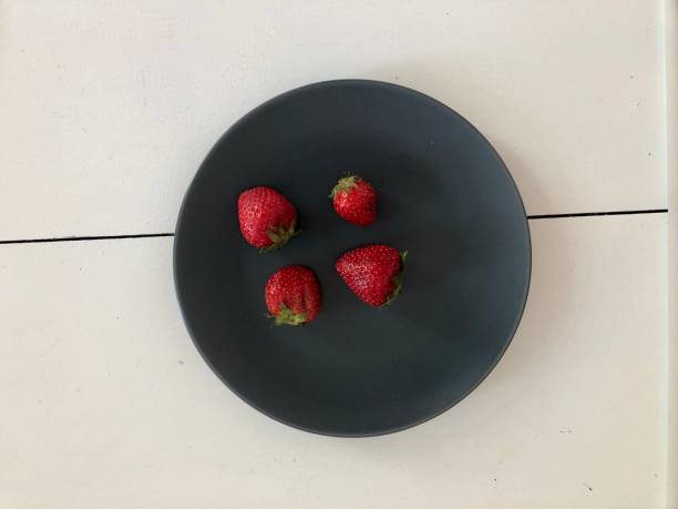 istock Four Strawberries on a Round Black Plate 1150098801