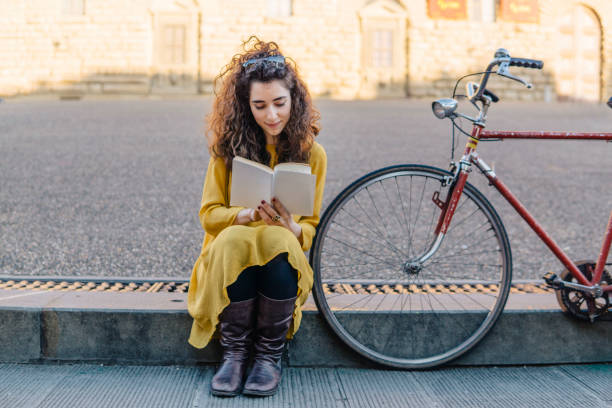 Young woman reading a book outdoor close to her bike