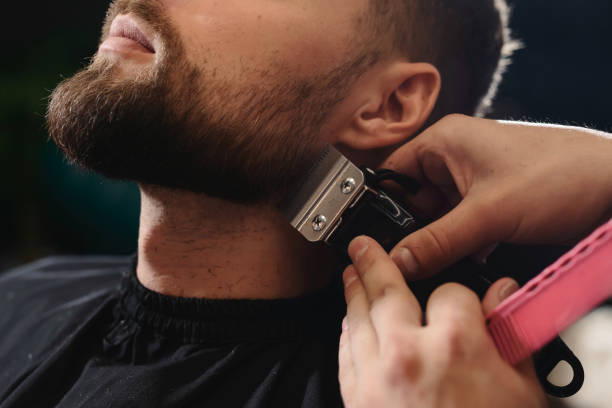 istock Getting perfect shape. Close-up side view of young bearded man getting beard haircut by hairdresser or barber at barbershop 1150113302