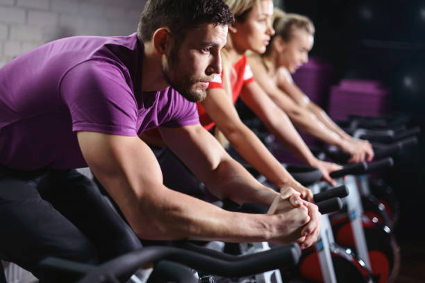 cerrar las manos del hombre en bicicleta en clase de spinning. grupo de amigos sonriendo en el gimnasio ejercitándose en bicicleta estática. felices atletas alegres entrenando en bicicleta estática. - gym machine smiling coach fotografías e imágenes de stock