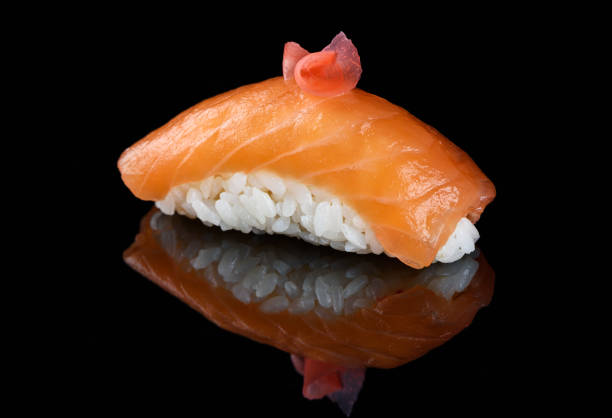 Sushi nigiri on a black mirror surface. The dish is decorated with a slice of pickled ginger. , rustic.
