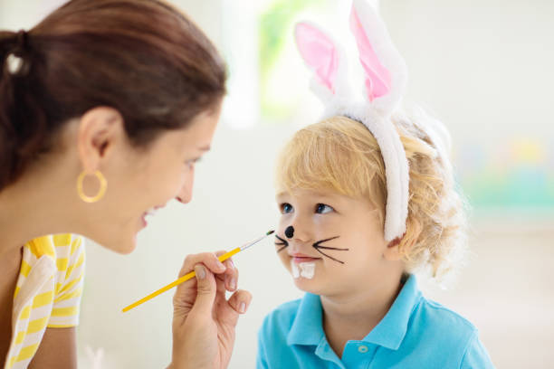 мать и дети, семейная раскраска пасхальных яиц. - face paint child paint rabbit стоковые фото и изображения