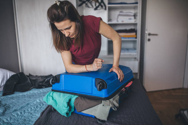 istock Young woman having trouble with over-packed suitcase 1150134752
