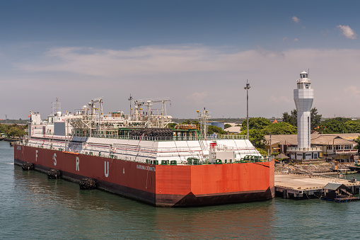 Bali, Indonesia - February 25, 2019: Red and white Floating Storage and Regasification Unit, FSRU, LNG-vessel in Benoa Harbour under light blue sky.