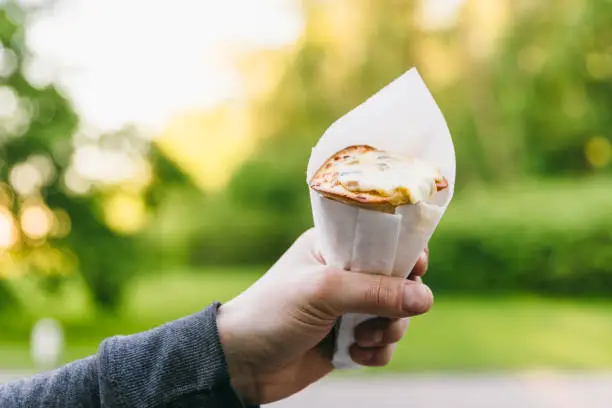 Close up hand hold pizza cone, streetfood in the green summer park