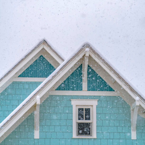 Clear Square Snow falling on a blue home in Daybreak Utah with cloudy sky in the background. The house has sliding glass window and snow covered roof in winter.