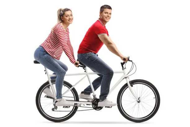 Full length shot of a young man and woman on a tandem bicycle looking at the camera isolated on white background