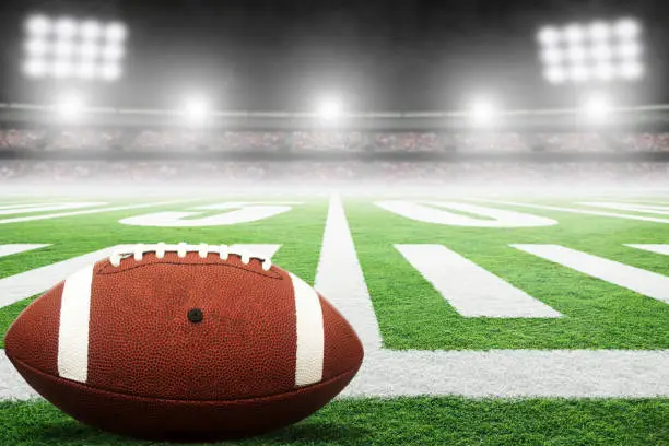 Close up of American football on fictitious stadium field with yard line markings and spotlight with blurred background and copy space. Fictitious stadium created in Photoshop.