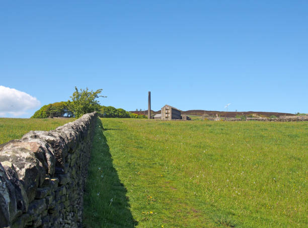 istock a long stone wall in perspective bordering a green grass meadow in bright spring sunlight with a historic abandoned mill and the village of old old town next to midgley moor in west yorkshire 1150167034