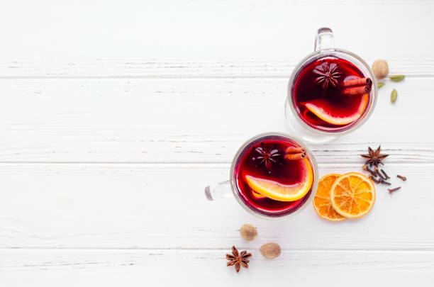 Mulled wine with orange Two glasses of hot red mulled wine or gluhwein with orange, cinnamon sticks and anise on white wooden background. Spicy warm beverage. Seasonal mulled drink. Top view. Copy space. mulled wine photos stock pictures, royalty-free photos & images