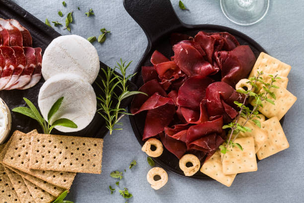 イタリアの bresaola は、青いリネンのお祝いのテーブルクロスの上に芳香族のハーブと白ワイン、クラッカー、グリッシーニとタラーリとテーブルの上にトレイにスライスを務めました。 - tomino ストックフォトと画像