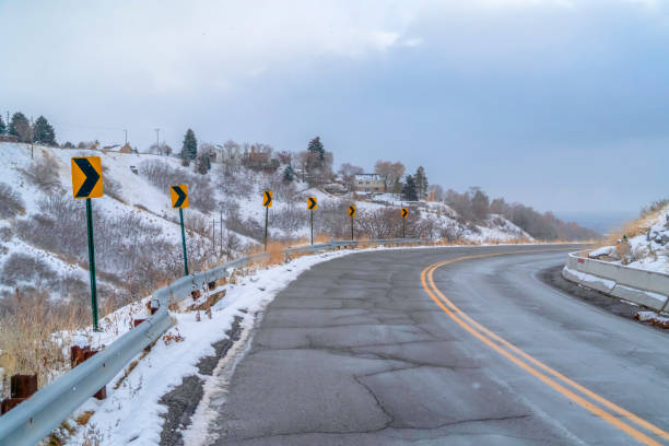 Damaged mountain road with directional road signs. A damaged road curving through a snowy mountain in winter.