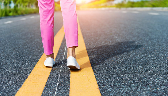 Woman legs walking on asphalt road.