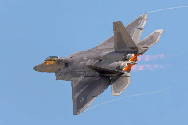 F-22 Raptor in a  high G maneuver, with condensation trails forming  at the wings tip and afterburners on