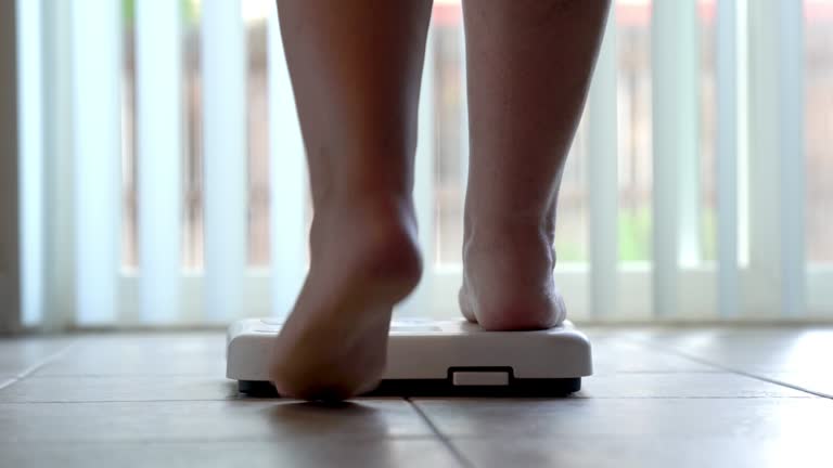 Bare feet and legs of a woman stepping onto a bathroom scale to check her weight