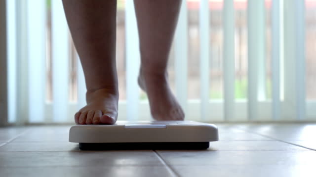 Bare feet and legs of a woman stepping onto a bathroom scale to check her weight