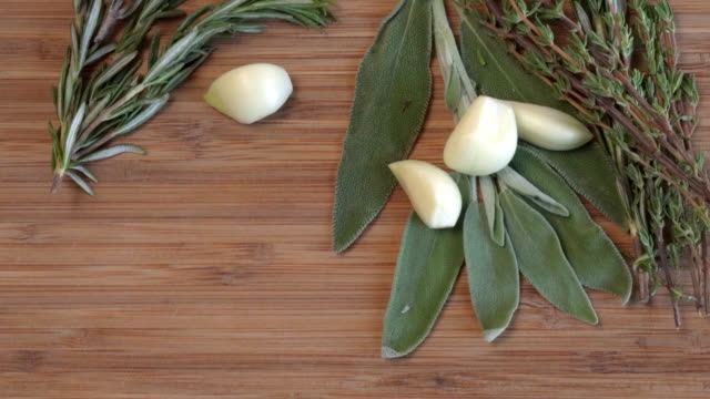 A Video Clip Of Aromatic Herbs, Garlic Cloves, Rosemary, Sage And Thyme Displayed On A Wood Cutting Board