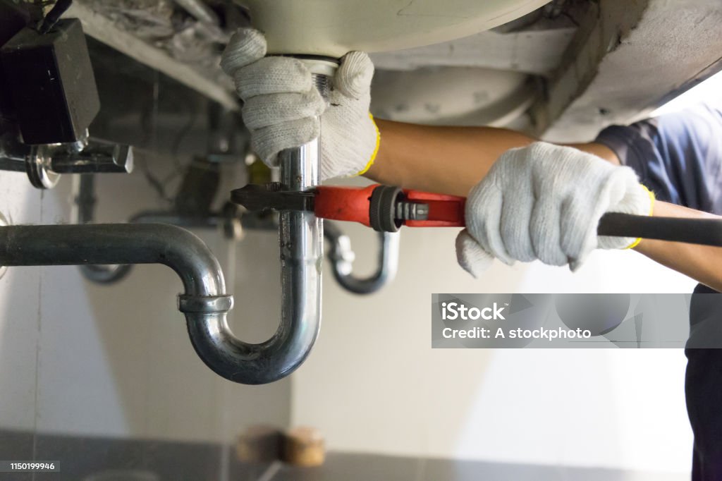Plumber fixing white sink pipe with adjustable wrench. Plumber Stock Photo
