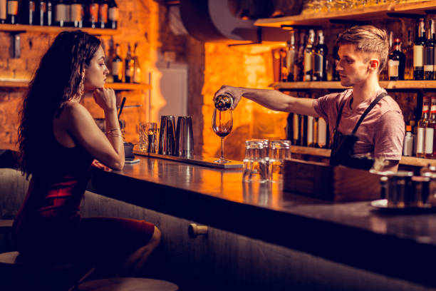 Barman pouring red wine for woman sitting at the bar counter