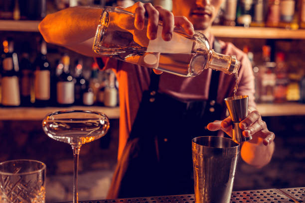 Barman wearing black apron pouring vodka for cocktail Pouring vodka. Professional experienced barman wearing black apron pouring vodka for cocktail cocktail bar busy stock pictures, royalty-free photos & images