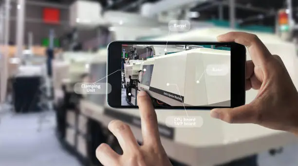 Augmented reality concept. AR. Industrial 4.0 , Hand of engineer holding mobile smart phone using virtual AR to check the work of electric machine on smart factory background.