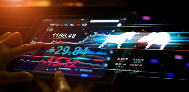 A businessman using a tablet mobile device to check and analyzing market data with bull and bear shapes symbols of stock market trends on them, stock market exchange on interface virtual screen. un empresario que utiliza una tableta dispositivo móvil para comprobar y analizar los datos del mercado con los símbolos de toro y oso formas de las tendencias del mercado de valores en ellos, el mercado bursátil en la pantalla virtual de interfaz.