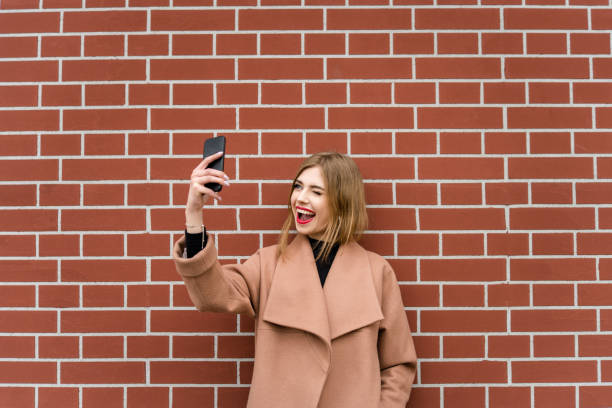 istock Smiling woman makes selfie at brick wall 1150216336