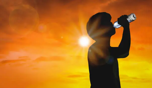 Photo of Silhouette man is drinking water bottle on hot weather background with summer season. High temperature and heat wave concept.