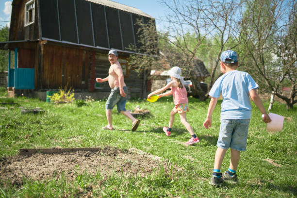 A family (father, daughter and her cousin boy) spends fun a weekend in a rural cottage. The children are pouring water on the man from a buckets. The middle-aged man is running away from children. Shooting on yard of a rural cottage at sunny hot spring day